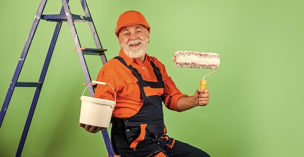 Ein echter Bauarbeiter, ein älterer Mann, verwendet eine Walze auf einer Leiter, die in der Wohnung arbeitet