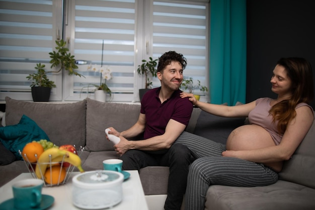 Ein Ehemann massiert die Füße seiner Frau und sie sitzen zusammen auf dem Sofa im Wohnzimmer Schwangere