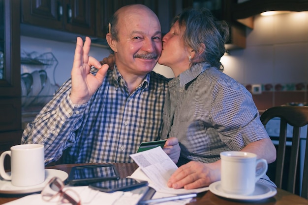 Ein Ehepaar zählt Geld und ein Budget. Die Frau küsst die Wange ihres Mannes. Er zeigt das Okay-Zeichen