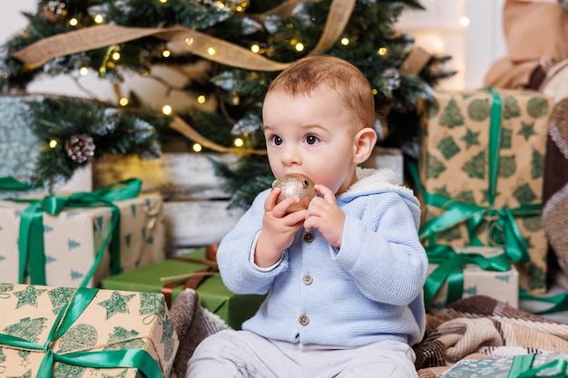 Ein einjähriger Junge sitzt in der Nähe eines geschmückten Weihnachtsbaums mit Geschenken Weihnachtsbaum im Haus Ein glückliches Kind wartet auf das neue Jahr