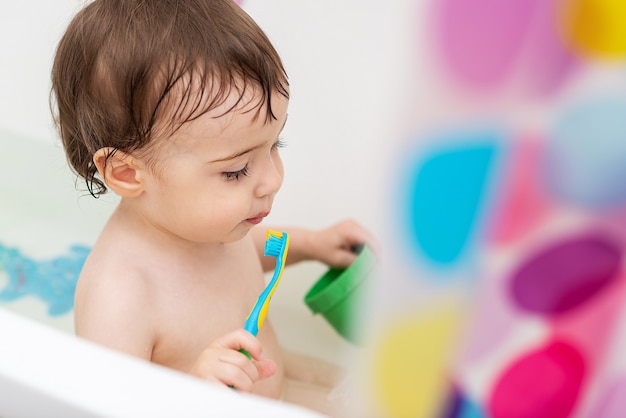 Ein einjähriges Baby wäscht sich in der Badewanne spielt mit Spielzeug und lernt Zähneputzen