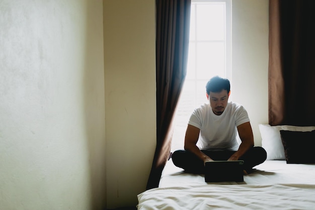 Ein einsamer Mann sitzt und ruht allein in einem dunklen Schlafzimmer mit Licht vom Vorhang