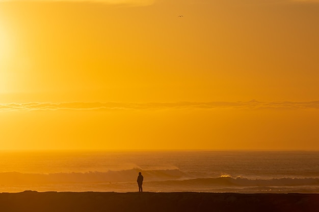 Ein einsamer Mann steht am Meer bei leuchtend orangefarbenem Sonnenuntergang