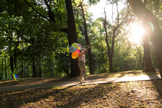 Ein einsamer Rentner geht mit Luftballons den Weg im Park entlang Ein älterer Mann hat Spaß im Park zwischen den Bäumen