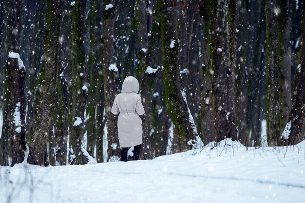 Ein einsames Mädchen geht im Winter während eines Schneefalls im Park spazieren