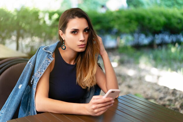 Ein einsames trauriges kaukasisches Mädchen sitzt in einem offenen Sommercafé mit einem Telefon