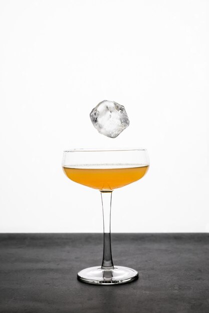 Ein Eiswürfel, der mit einem Orangencocktail in ein Coupéglas fällt