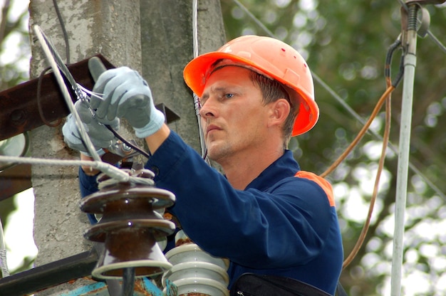 Ein Elektriker an einem Strommast wechselt einen beschädigten Isolator