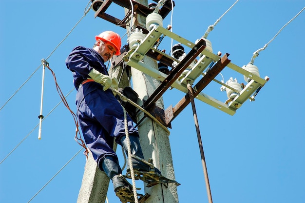 Ein Elektriker an einer Stange vergründet die Leitungen einer Stromleitung gegen einen blauen Himmel