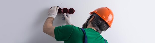 Ein Elektriker installiert Steckdosen in der Wohnung. Ein Typ mit orangefarbenem Helm und Overall macht Elektrik im Haus