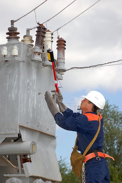 Ein Elektriker misst die Spannung an einer Stromleitung, bevor er ein Umspannwerk repariert