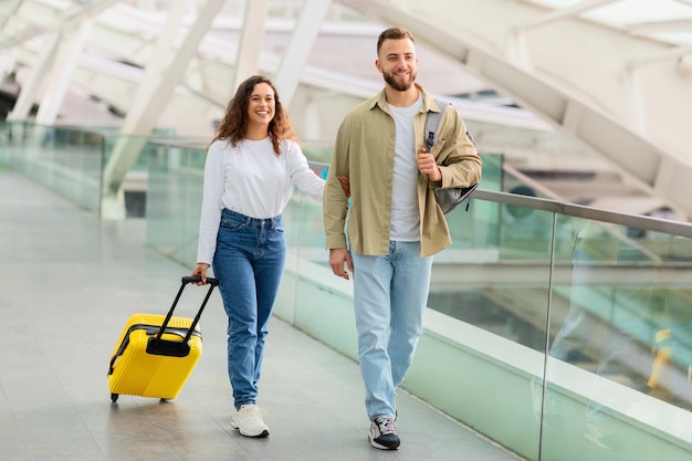 Ein entspanntes junges Paar geht beiläufig mit Gepäck durch das Flughafenterminal