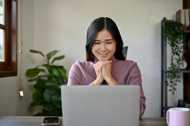 Ein entzückendes asiatisches Mädchen benutzt einen Laptop, schaut auf den Laptop-Bildschirm und entspannt sich zu Hause.