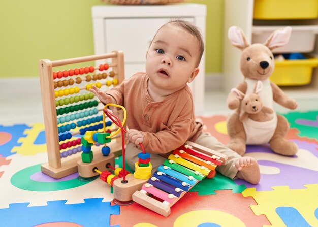 Ein entzückendes hispanisches Kleinkind spielt Xylofon und sitzt im Kindergarten auf dem Boden