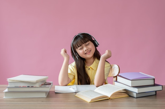 Ein entzückendes junges asiatisches Mädchen hört an ihrem Schreibtisch gerne Musik über ihre Kopfhörer