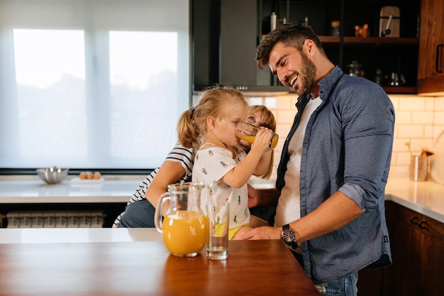 Ein entzückendes kleines Mädchen und ihre Eltern trinken zusammen Saft zu Hause