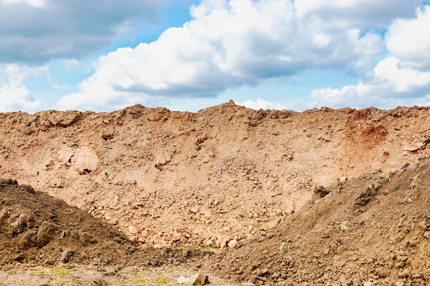 Ein Erdhaufen, der aus einem Graben gegen einen blauen bewölkten Himmel gegraben wurde Erdarbeiten auf der Baustelle