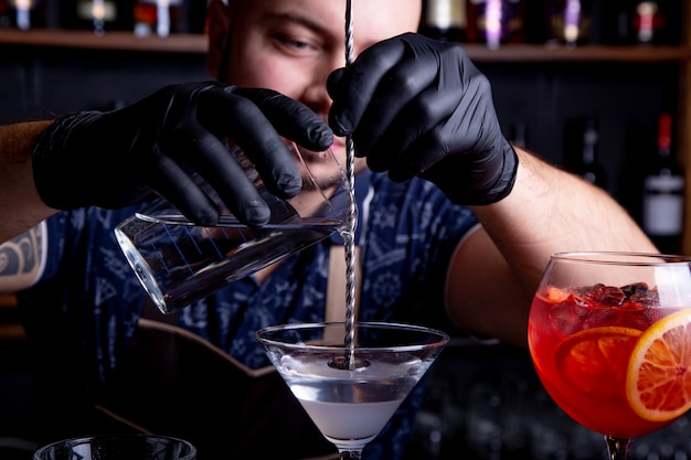 Ein erfahrener Barmann macht einen Cocktail im Nachtclub. Professioneller Barkeeper bei der Arbeit in der Bar, die süßes Getränk in Glas auf Party im Nachtclub gießt. Barmann dekoriert Cocktail.