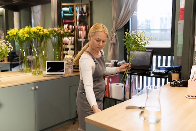 Ein erfahrener Florist wickelt einen Gänseblümchenzweig in Geschenkpapier