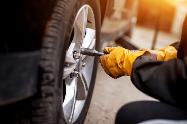 Ein erfahrener, hart arbeitender Mechaniker in orangefarbenen Handschuhen verwendet einen elektrischen Schraubenschlüssel, um die Schrauben in einem Autorad festzuziehen.