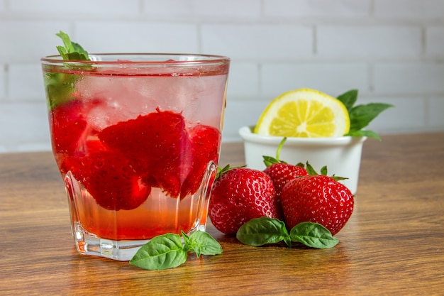 Ein erfrischendes Sommergetränk mit Eis, Erdbeeren und Zitrone auf Holz. Das Konzept des Fruchtgetränks.