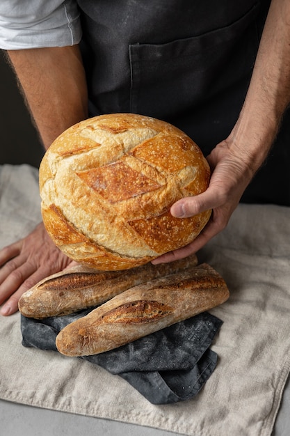 Ein erwachsener europäischer Bäcker hält ein rundes frisches Brot in den Händen, ein Mann in einer Bäckerei hält ein