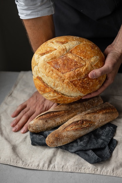 Ein erwachsener europäischer Bäcker hält ein rundes frisches Brot in den Händen, ein Mann in einer Bäckerei hält ein