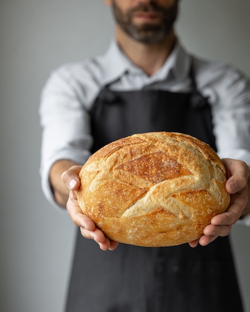 Ein erwachsener europäischer Bäcker hält ein rundes frisches Brot in den Händen ein Mann in einer Bäckerei hefefrei