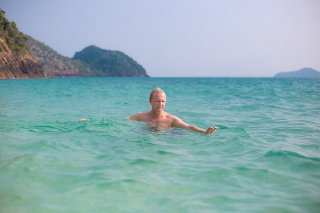 Ein erwachsener europäischer Mann schwimmt im azurblauen Meerwasser auf einer tropischen Insel. Reisen und Tourismus an Sommerferientagen.