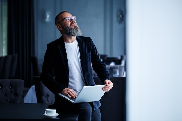 Ein erwachsener Geschäftsmann mit Bart in Brille sitzt mit einem Laptop auf dem Schoß und arbeitet. Der Regisseur erstellt einen Zeitplan für den Workflow