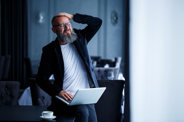 Ein erwachsener Geschäftsmann mit Bart in Brille sitzt mit einem Laptop auf dem Schoß und arbeitet. Der Regisseur erstellt einen Zeitplan für den Workflow