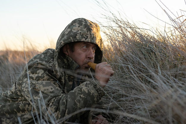 Ein erwachsener Jäger mit einem Gewehr lockt Enten mit einem Köder an, während er im Schilf sitzt