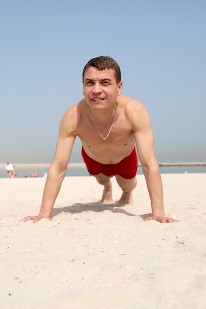 Ein erwachsener kaukasischer Mann im Alter von 35 bis 40 Jahren treibt Sport, Liegestütze auf Sand unter der strahlenden Sonne.