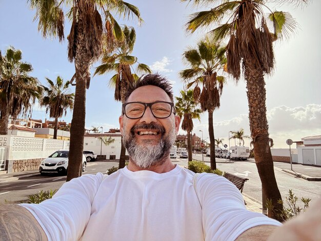 Ein erwachsener Mann macht ein Selfie bei einer Freizeitaktivität im Freien und geht auf der Straße in einem tropischen, landschaftlich reizvollen Ort mit Palmen im Hintergrund.