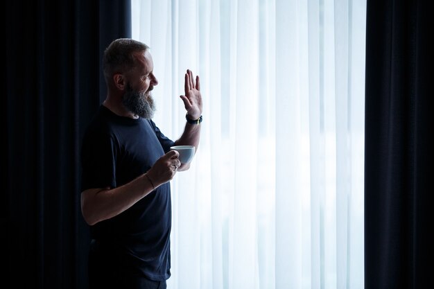 Ein erwachsener Mann mit Bart trinkt Kaffee und schaut aus dem Fenster. Erholungskonzept für den Arbeitstag