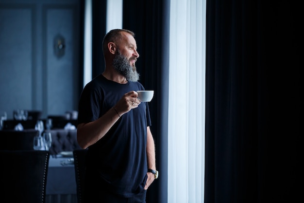 Ein erwachsener Mann mit Bart trinkt Kaffee und schaut aus dem Fenster. Erholungskonzept für den Arbeitstag