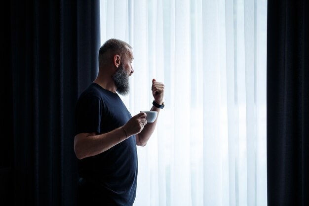 Ein erwachsener Mann mit Bart trinkt Kaffee und schaut aus dem Fenster. Erholungskonzept für den Arbeitstag