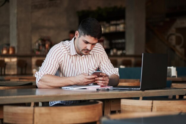 Ein erwachsener Mann sitzt tagsüber im Café und benutzt den Laptop für die Remote-Arbeit.