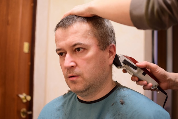 Ein erwachsener Mann wird mit einer Haarschneidemaschine getrimmt und sitzt vor der Kamera. Vielleicht zu Hause im Lockdown