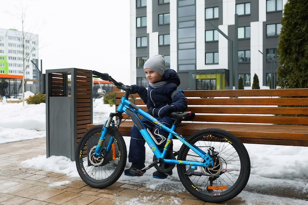 Ein europäischer Junge in einer Winterjacke ist es leid, Fahrrad zu fahren
