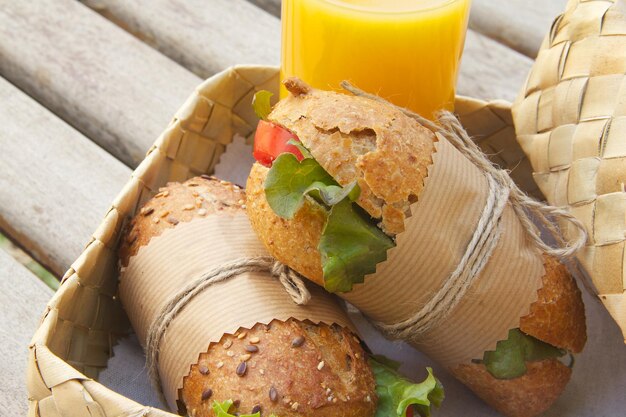 Foto ein express-mittagessen unter freiem himmel für vegetarier – vollkornbrötchen mit frischem gemüse und einem glas frischem orangensaft. im geflochtenen birkenkorb sind brötchen versteckt