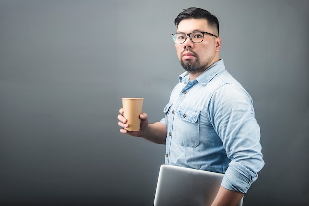 Ein fälliger Mann, der einen Computer und einen Kaffee anhält