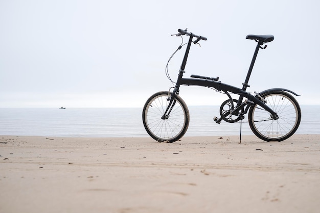 Ein Fahrrad steht an einem Sandstrand vor dem Hintergrund des Meeres und des Schiffes an bewölkten Tagen
