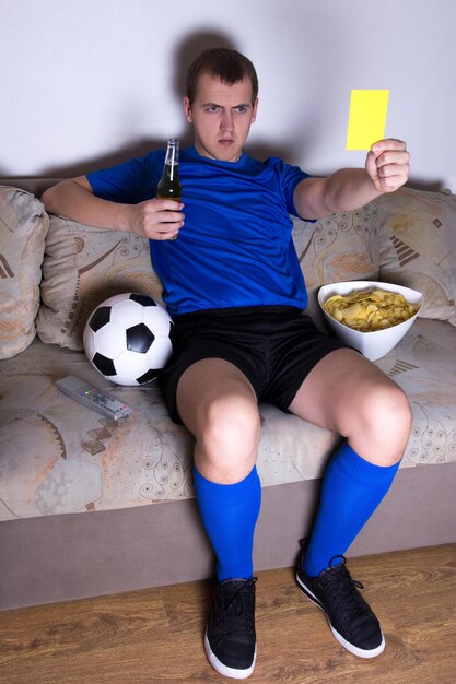 Ein fan schaut sich zu hause fußball im fernsehen an und zeigt die gelbe karte Premium-Foto