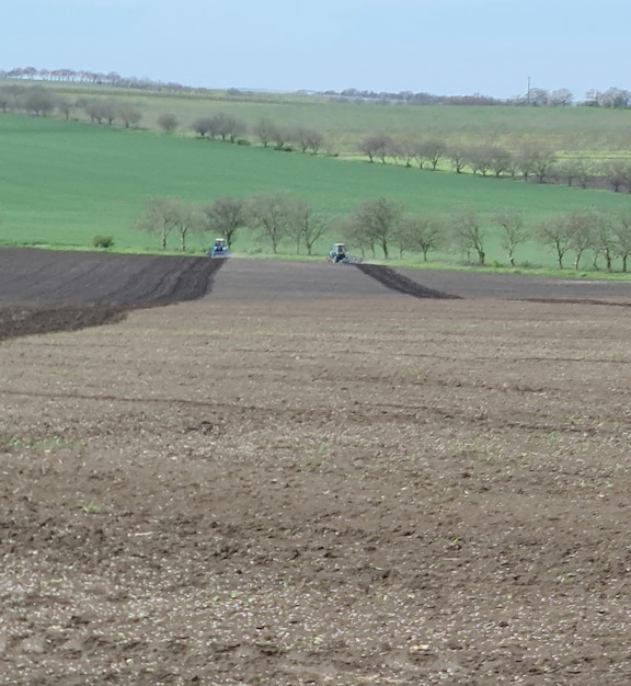 Ein Feld mit einem Traktor und ein Feld mit einer grünen Wiese im Hintergrund.