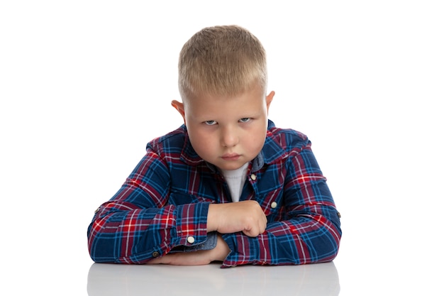 Ein fetter trauriger Junge sitzt am Tisch. Schüler in einem karierten Hemd. Zurück zur Schule. Isoliert. Nahansicht.