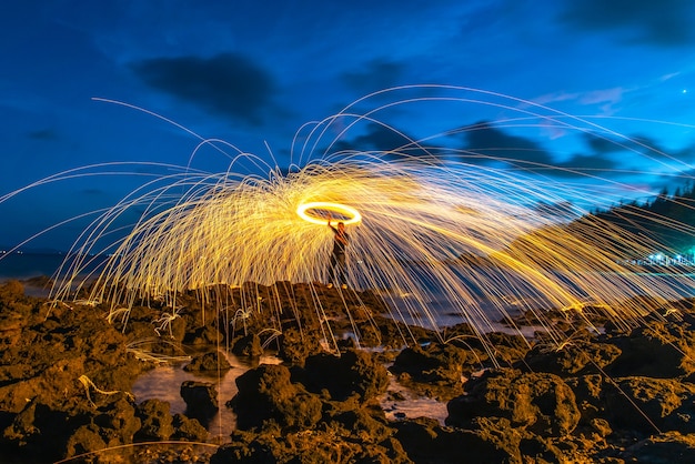 Ein Feuerring, der Stahlwolle auf dem Felsen und dem Strand spinnt.