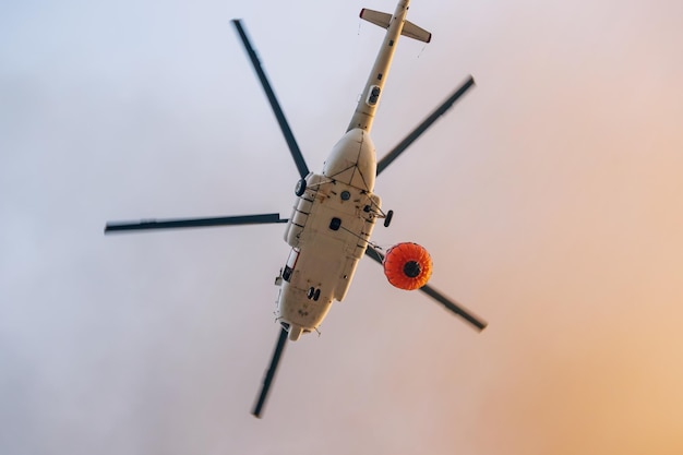 Ein Feuerwehrhelikopter fliegt zum Unfallort mit einem Korb mit Wasser gegen den Himmel.