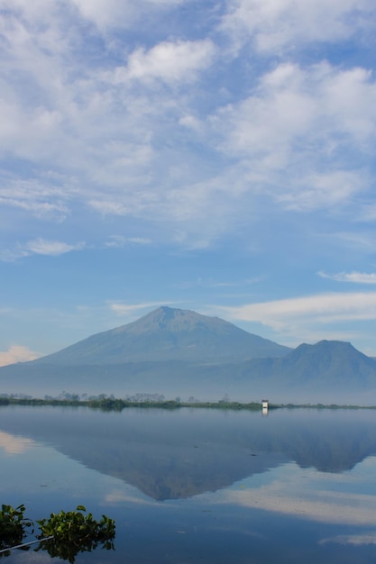 Foto ein fischer fängt fische mit einem holzkanu in rawa pening mit dem mount merbabu im hintergrund. holzkanu