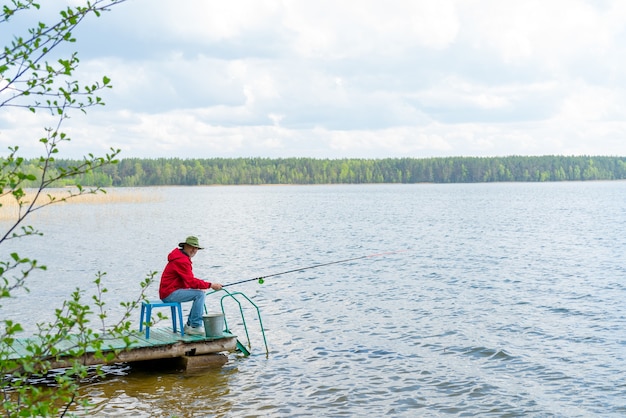 Ein Fischer mit Hut und Angelrute sitzt am Ufer des Flusses.